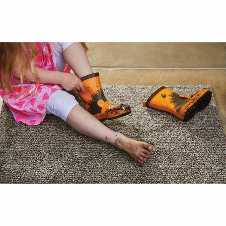 Child trying on orange rain boots with a cartoon design on a carpeted floor.