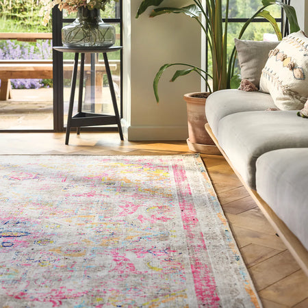 Living room with a colorful rug, gray sofa, and plants.