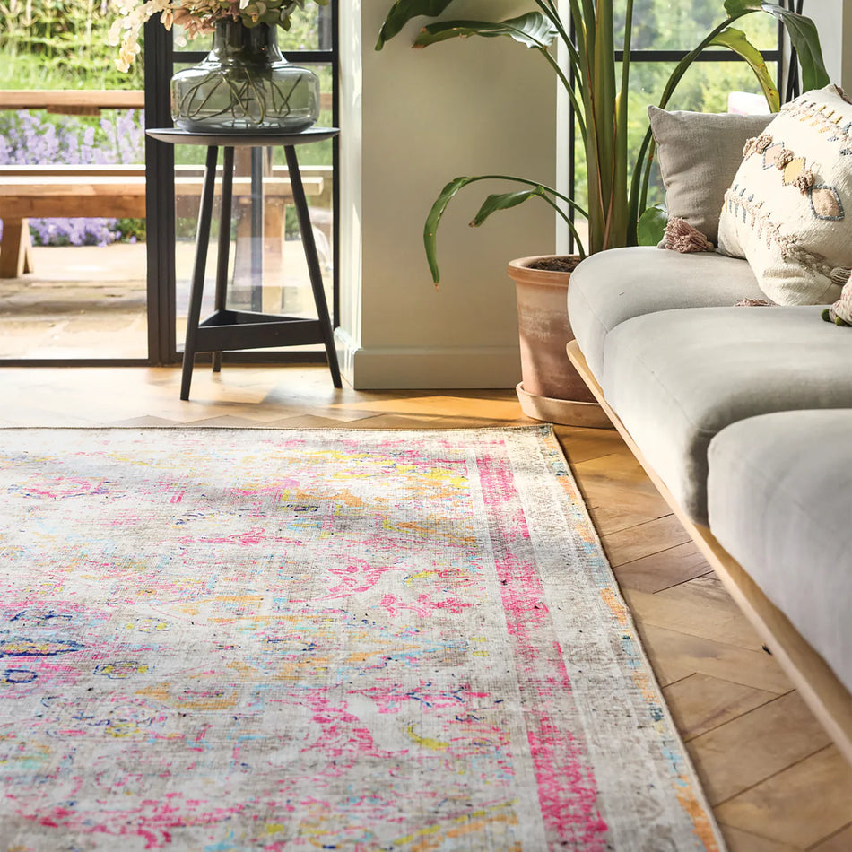Living room with a colorful rug, gray sofa, and plants.