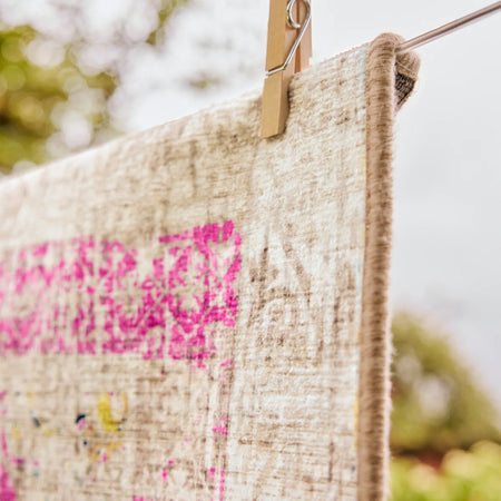 Textile with pink and multicolor design hanging on a clothesline with a blurred natural background
