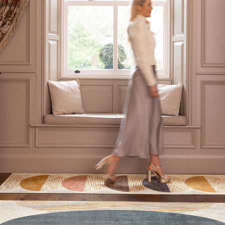 Woman walking past a window seat with cushions in a room with decorative wall paneling.