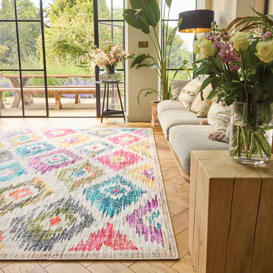 Living room with a colorful patterned rug, wooden coffee table, and floral arrangements.