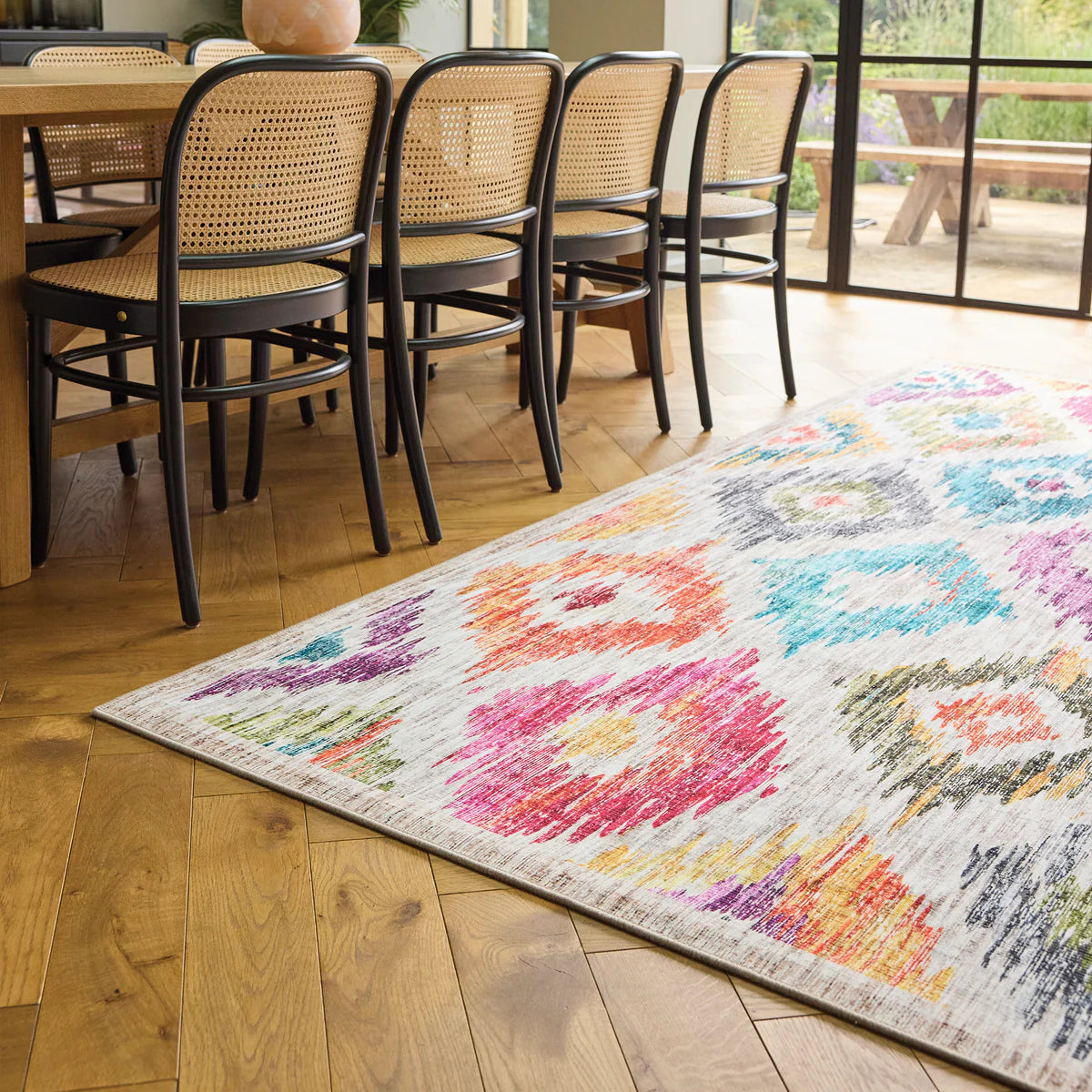 Colorful patterned rug on a wooden floor with chairs around a table.