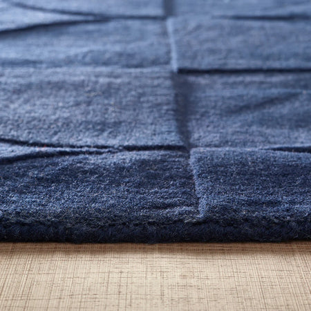 Close-up of Origins Penny Rug Infinity dark blue wool textured rug on a wooden floor