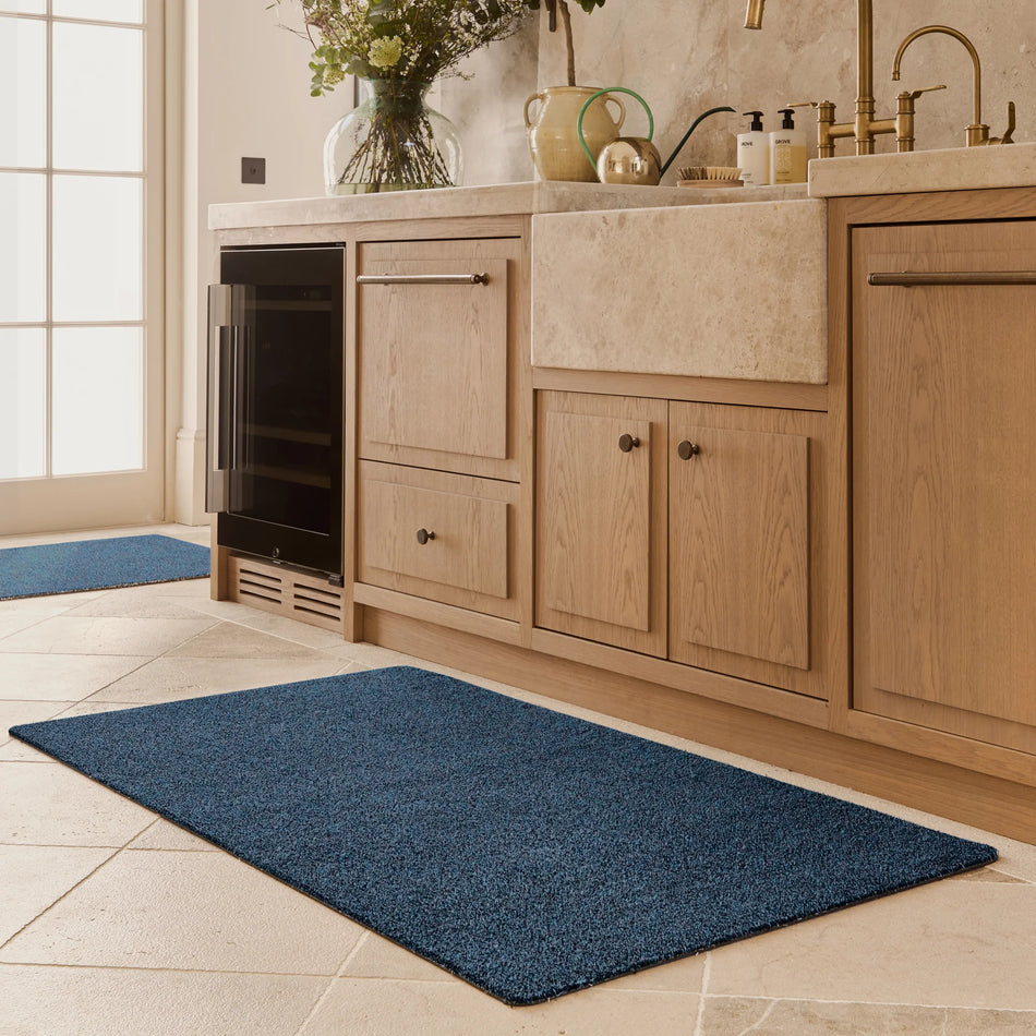 Blue mat on a tiled floor in a kitchen with wooden cabinets and a window.