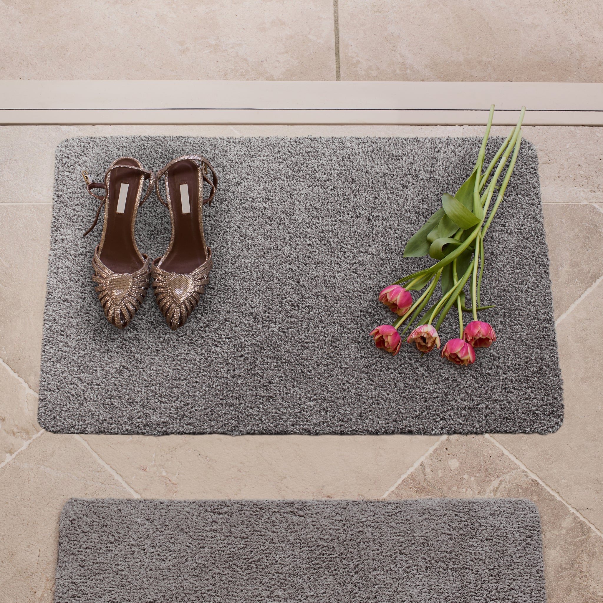 Gray doormat with shoes and flowers on a tiled floor