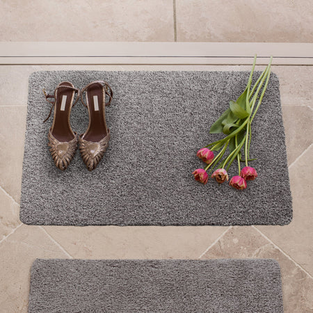 Gray doormat with shoes and flowers on a tiled floor