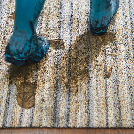 Blue shoes stepping onto a doormat with oil stains on a wooden floor.