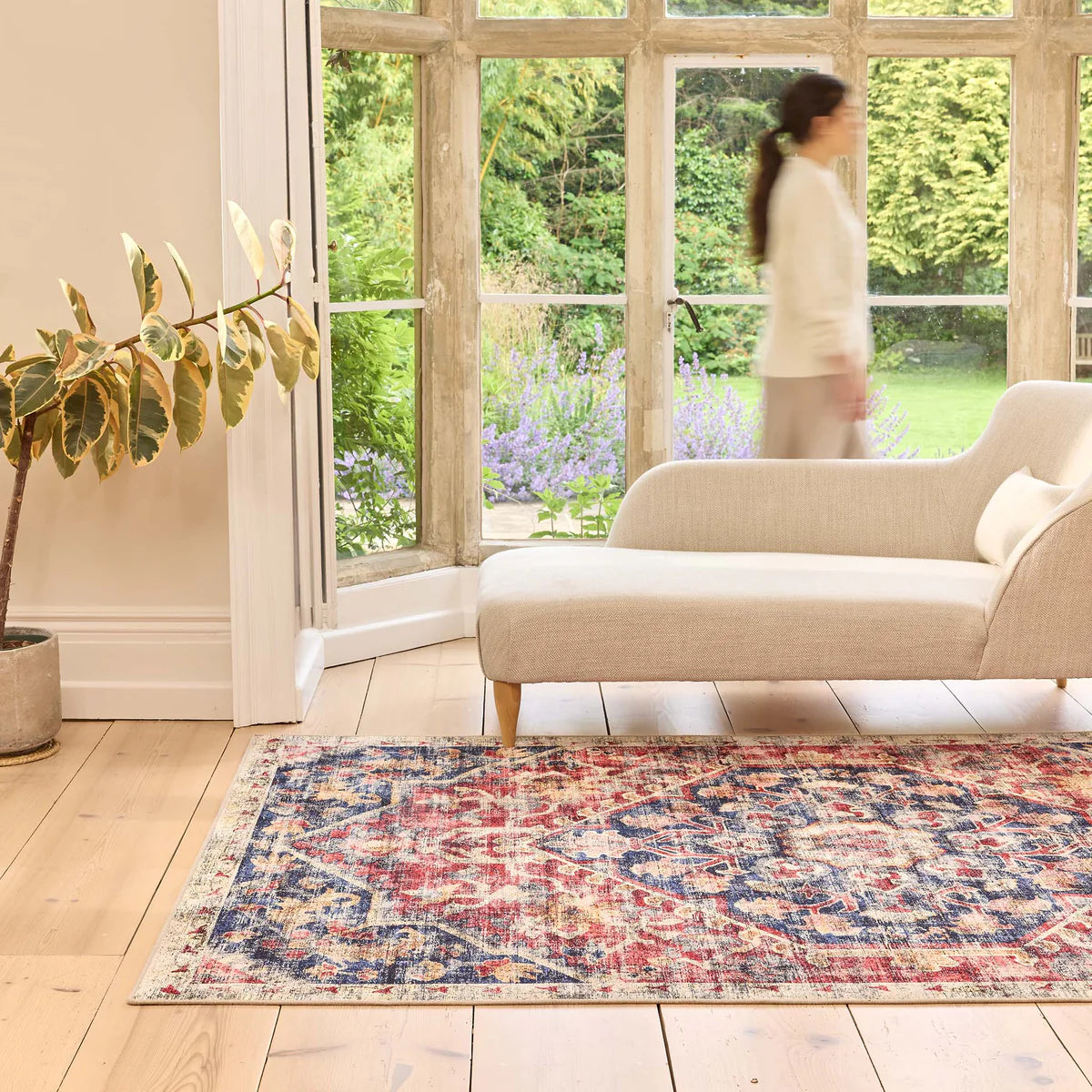 Living room with a patterned rug, beige sofa, and large windows showing a garden.
