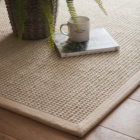 Sisal Boucle Beige woven mat on a wooden floor with a mug and book on top