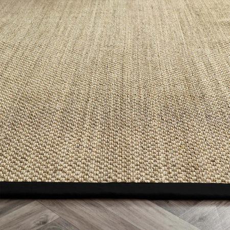 Close-up of a textured sisal beige rug with a black border on a wooden floor.