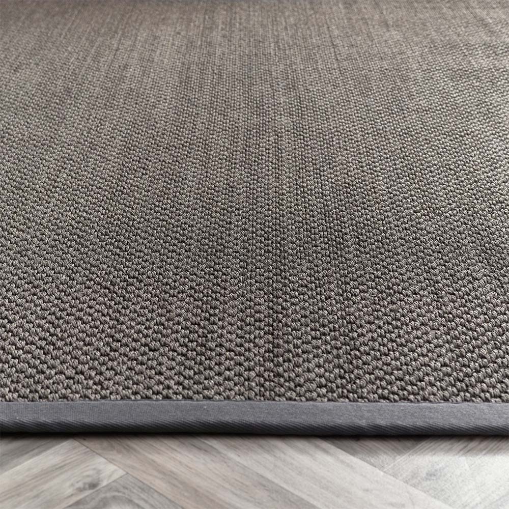 Close-up of a textured sisal dark grey with grey border rug on a wooden floor