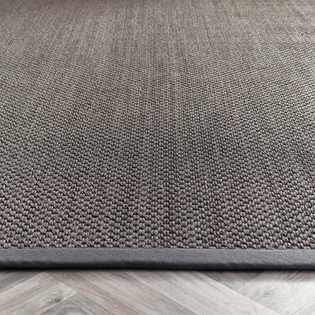 Close-up of a textured sisal dark grey with grey border rug on a wooden floor