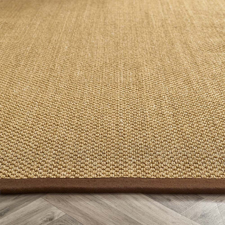 Close-up of a textured beige rug with a brown border on a wooden floor.