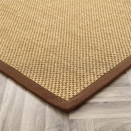 Beige woven rug with brown border on a wooden floor