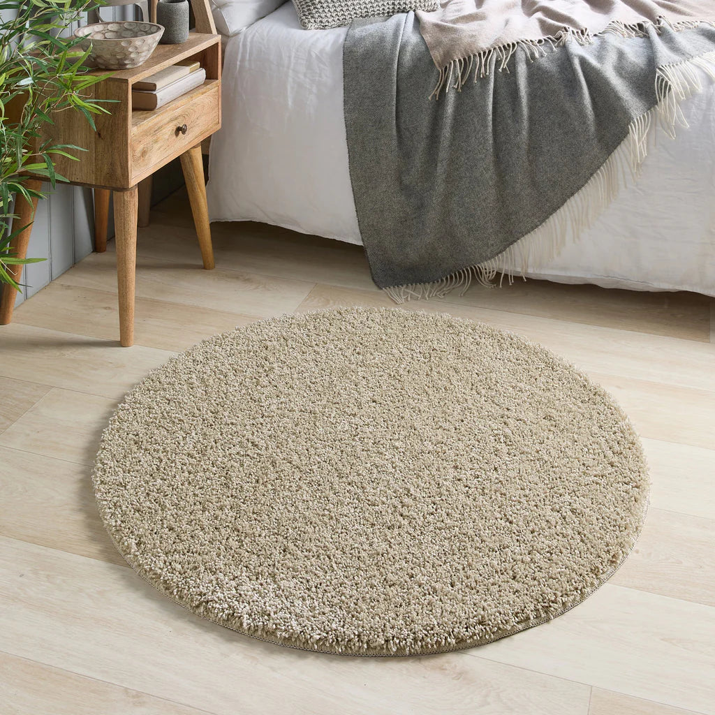 my rug Round beige rug on a wooden floor with a bed and side table in the background