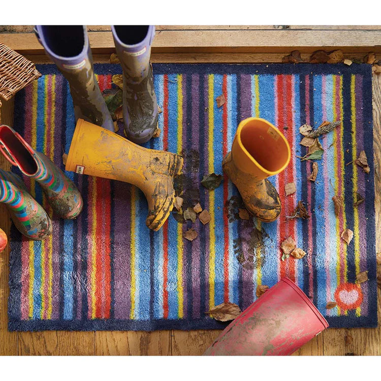 Colorful striped rug with muddy boots and a yellow bucket on a wooden floor.