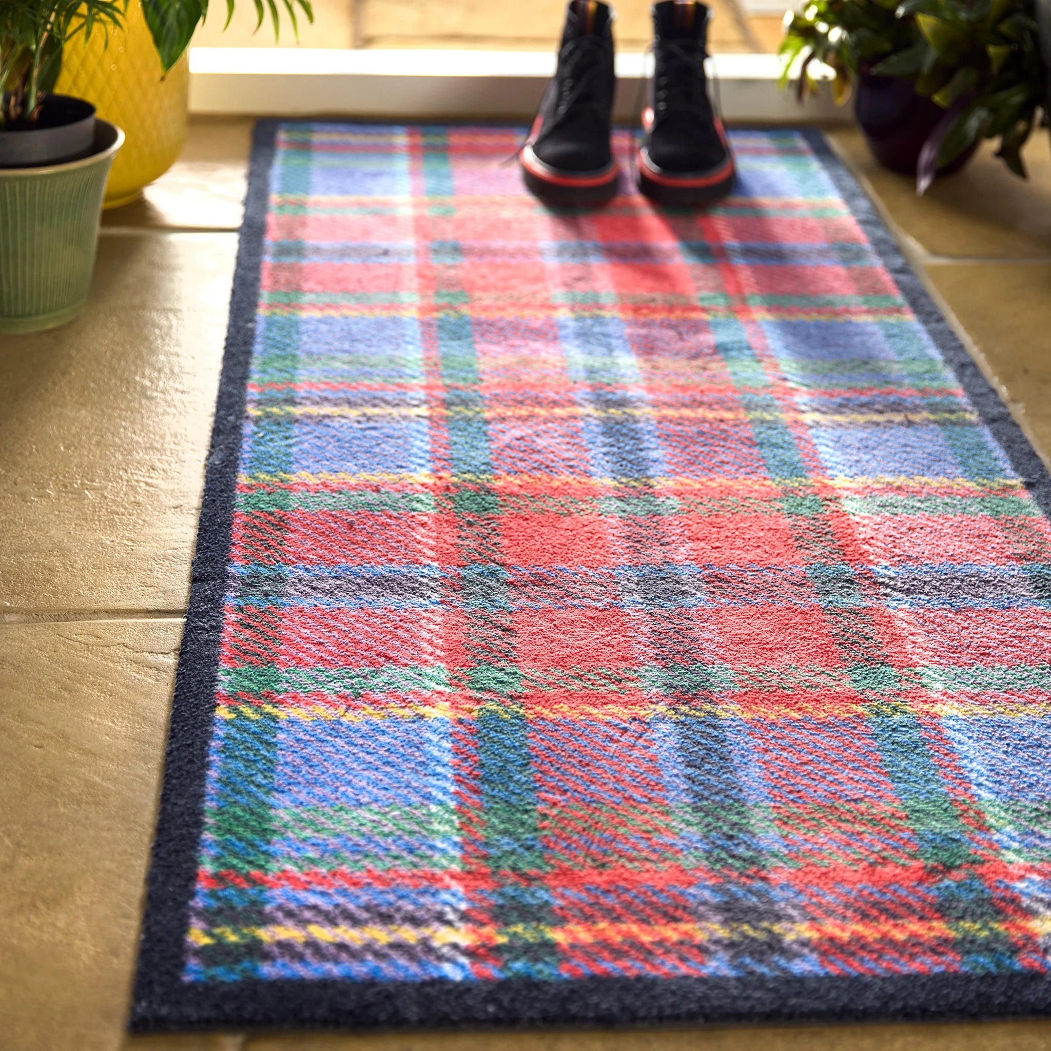 Colorful plaid rug on a wooden floor with shoes at the end