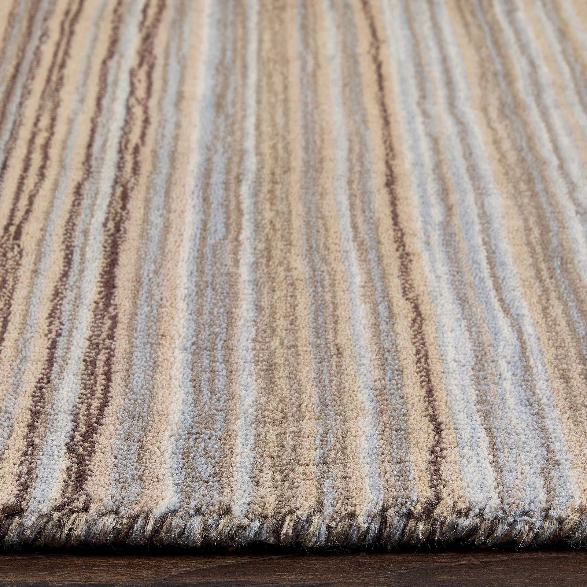 Close-up of a textured rug with horizontal stripes in brown, beige, and gray.