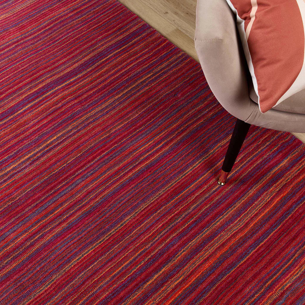 Origins Striped red and blue rug with a chair corner on a wooden floor.