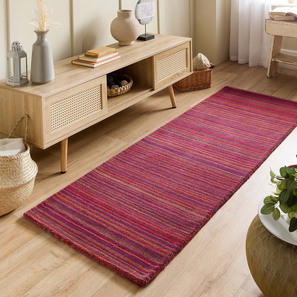 Long, Origins  multicolored striped rug on a wooden floor with a wooden console table in the background.