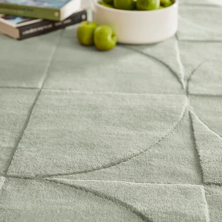 Close-up of a textured Origins Penny Rug Eucalyptus green wool rug with books and apples on top