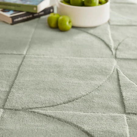 Close-up of a textured Origins Penny Rug Eucalyptus green wool rug with books and apples on top