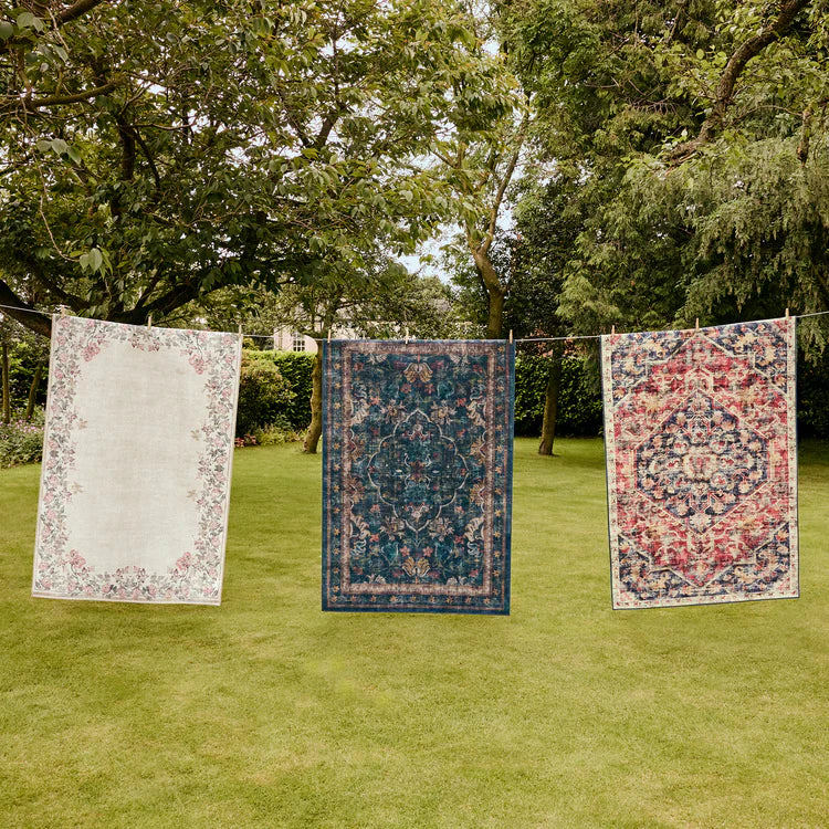 Three patterned rugs hanging on a line outdoors with trees in the background