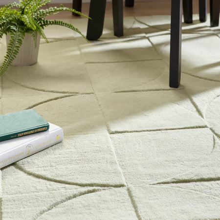Patterned Origins Penny Rug Eucalyptus green wool rug with books and a plant on a wooden floor